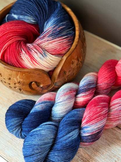 three skeins of red, white, and blue yarn in a wooden bowl