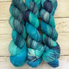 Blue and green skeins of yarn on a wooden surface