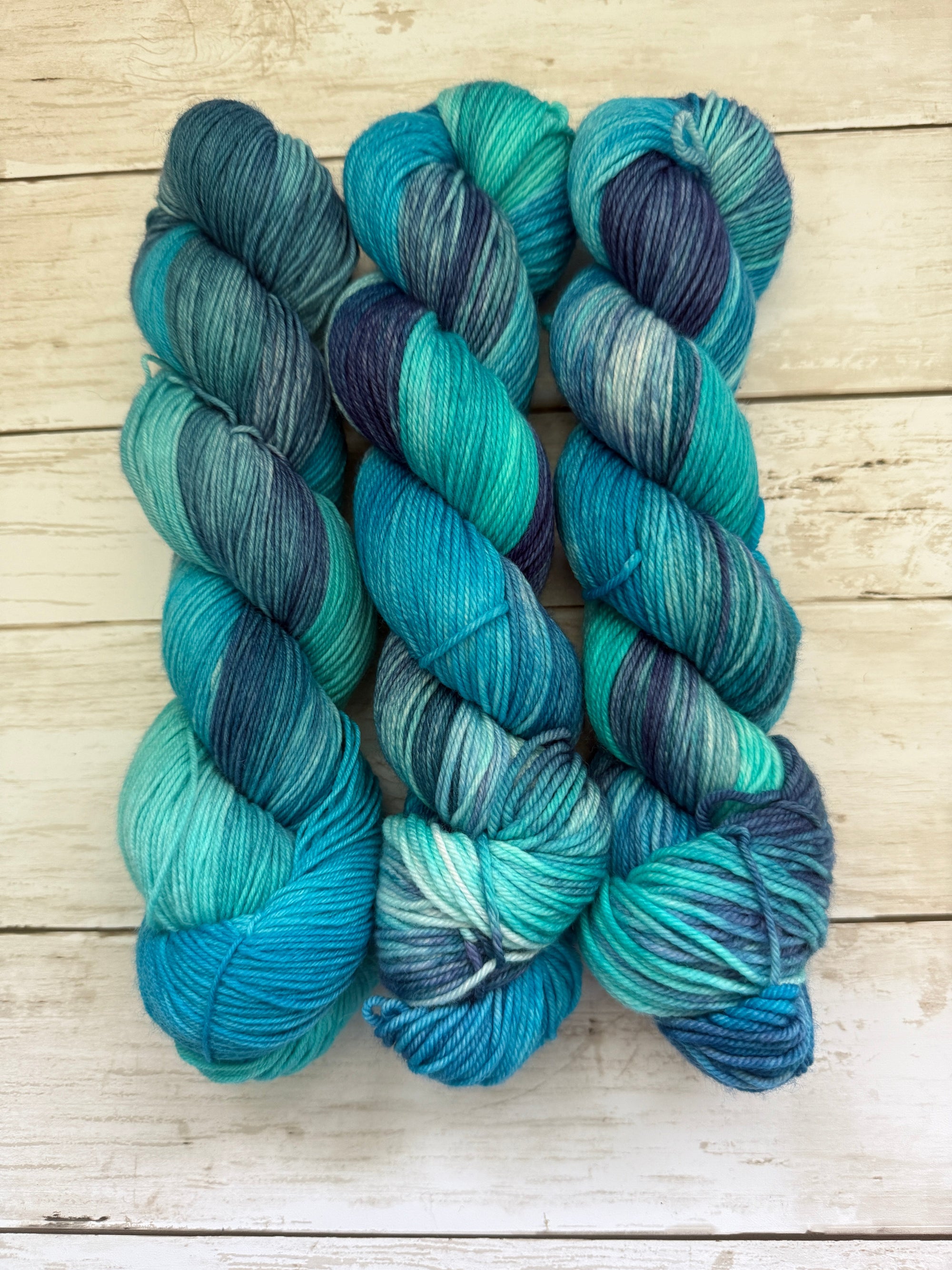 Blue and green skeins of yarn on a wooden surface