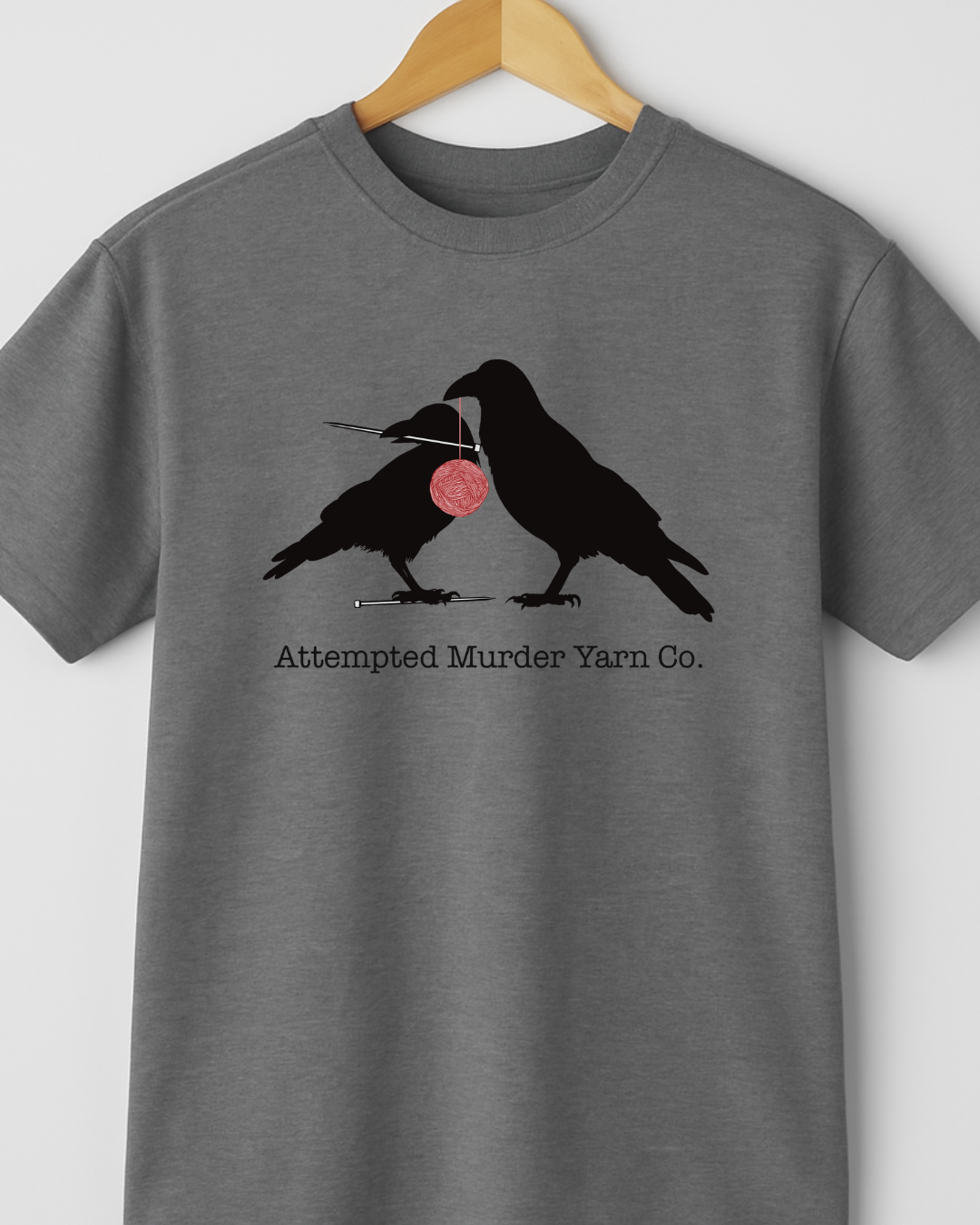 Gray t-shirt with crow design and 'Attempted Murder Yarn Co.' text on a hanger.