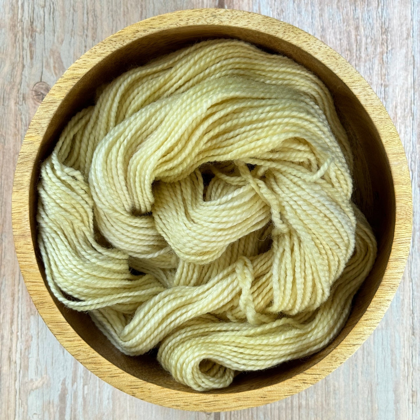 a wooden bowl filled with yarn on top of a wooden table