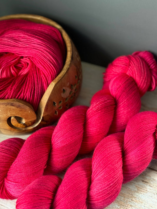 a pink skein of yarn next to a wooden bowl