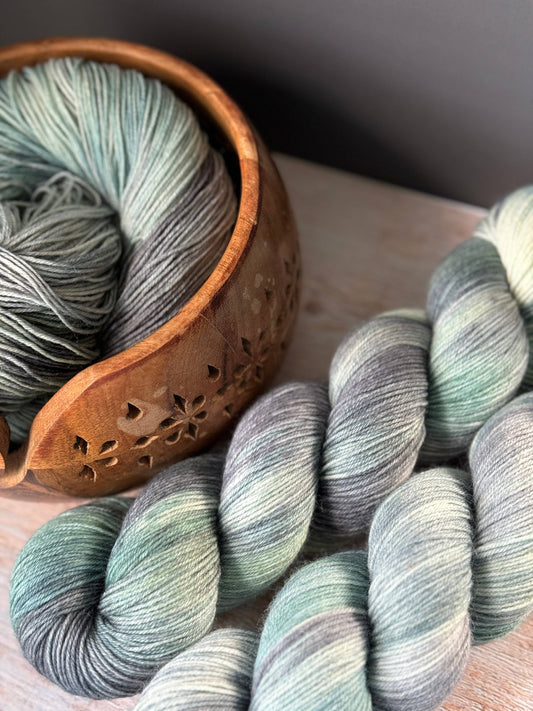 two skeins of yarn next to a wooden bowl