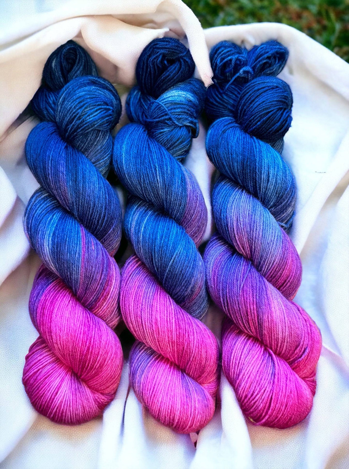 three skeins of blue and pink yarn on a white cloth