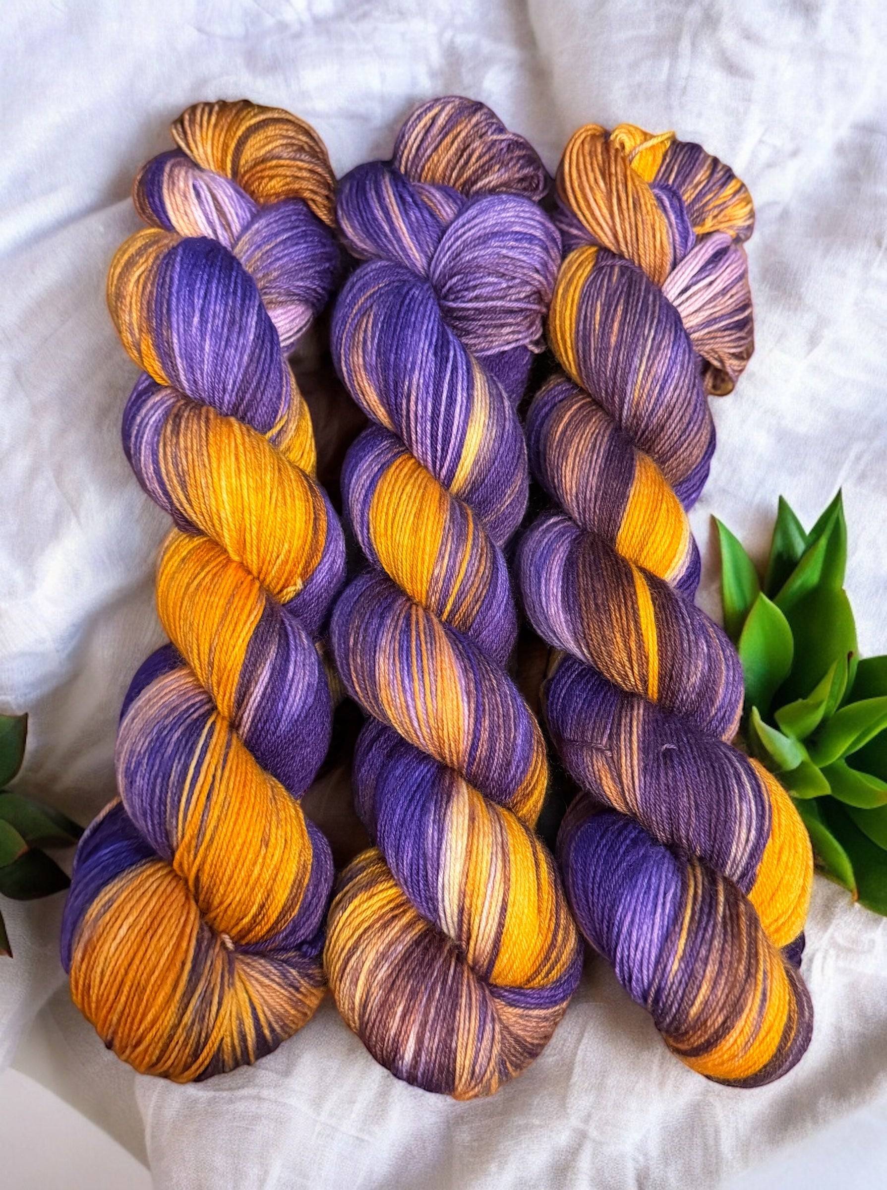 Three skeins of purple and gold yarn