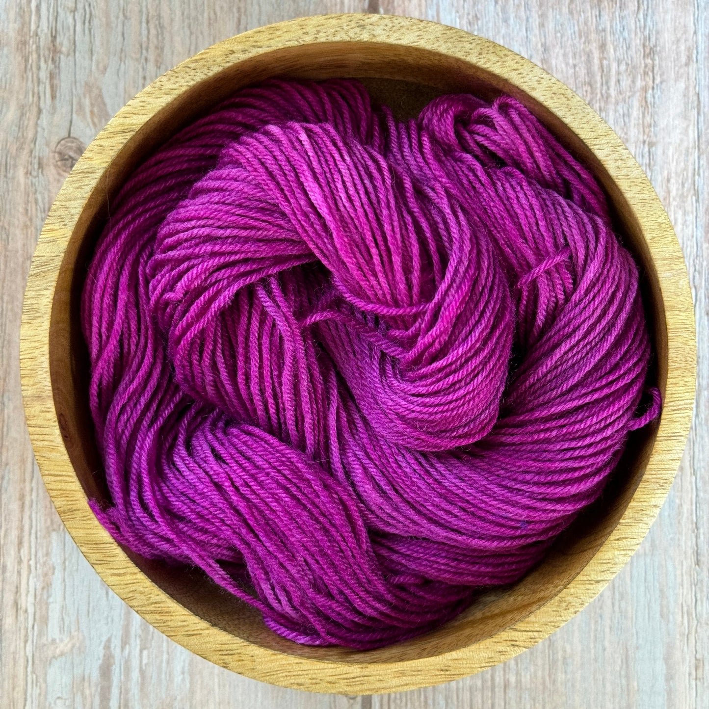 a purple skein of yarn in a wooden bowl