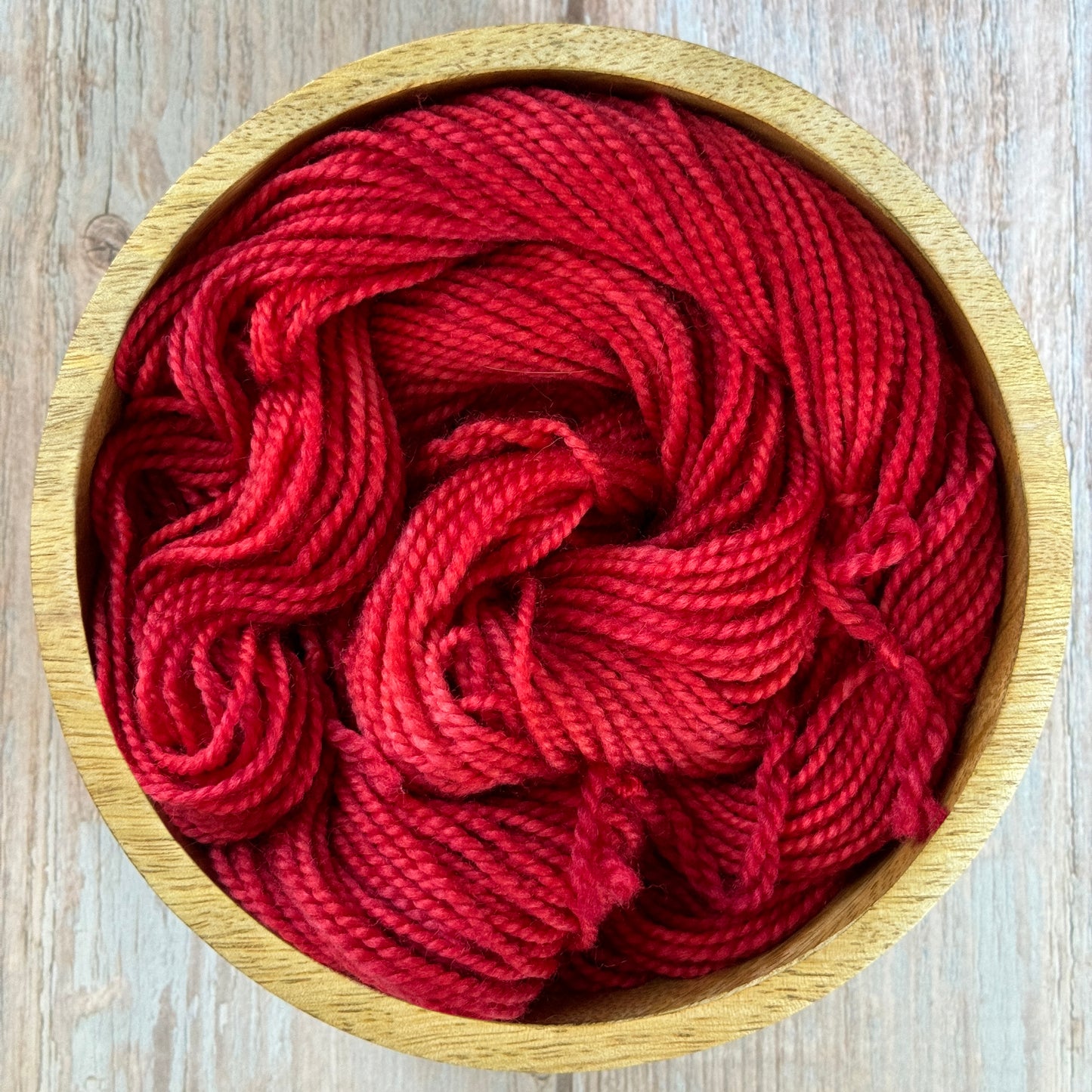 a wooden bowl filled with red yarn on top of a wooden table