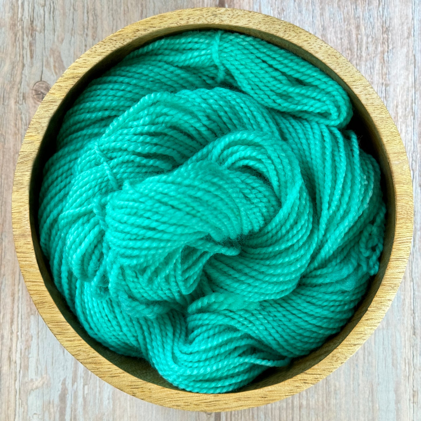 a green ball of yarn in a wooden bowl