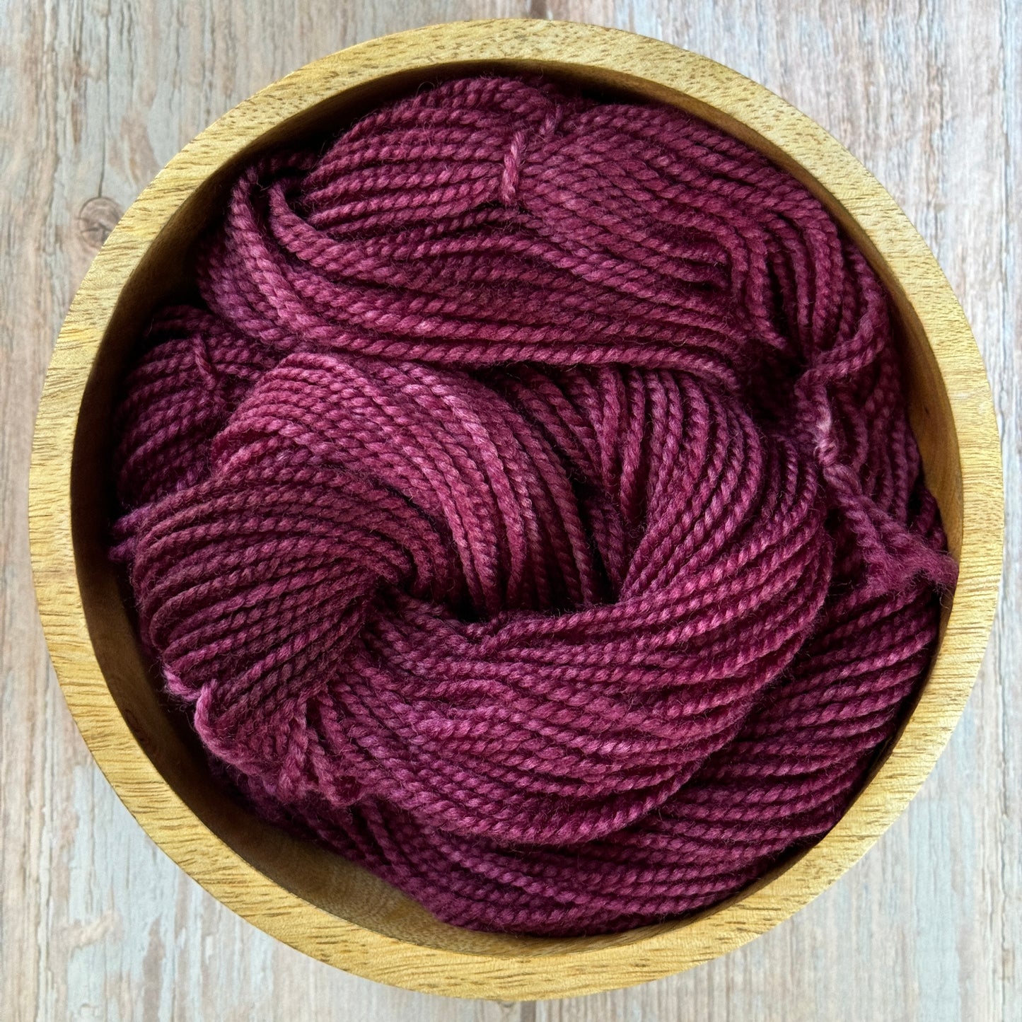 Burgundy yarn in a wooden bowl